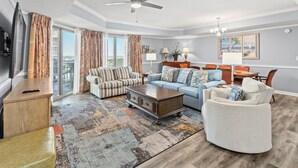 A spacious living room with a large sofa, a coffee table, and a dining area with chairs. - Royale Palms 1204 2 Br Oceanview in Kingston, Pool (Myrtle Beach)