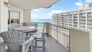 A balcony with a table and chairs, overlooking a building with balconies and a view of the ocean. - Royale Palms 1204 2 Br Oceanview in Kingston, Pool (Myrtle Beach)
