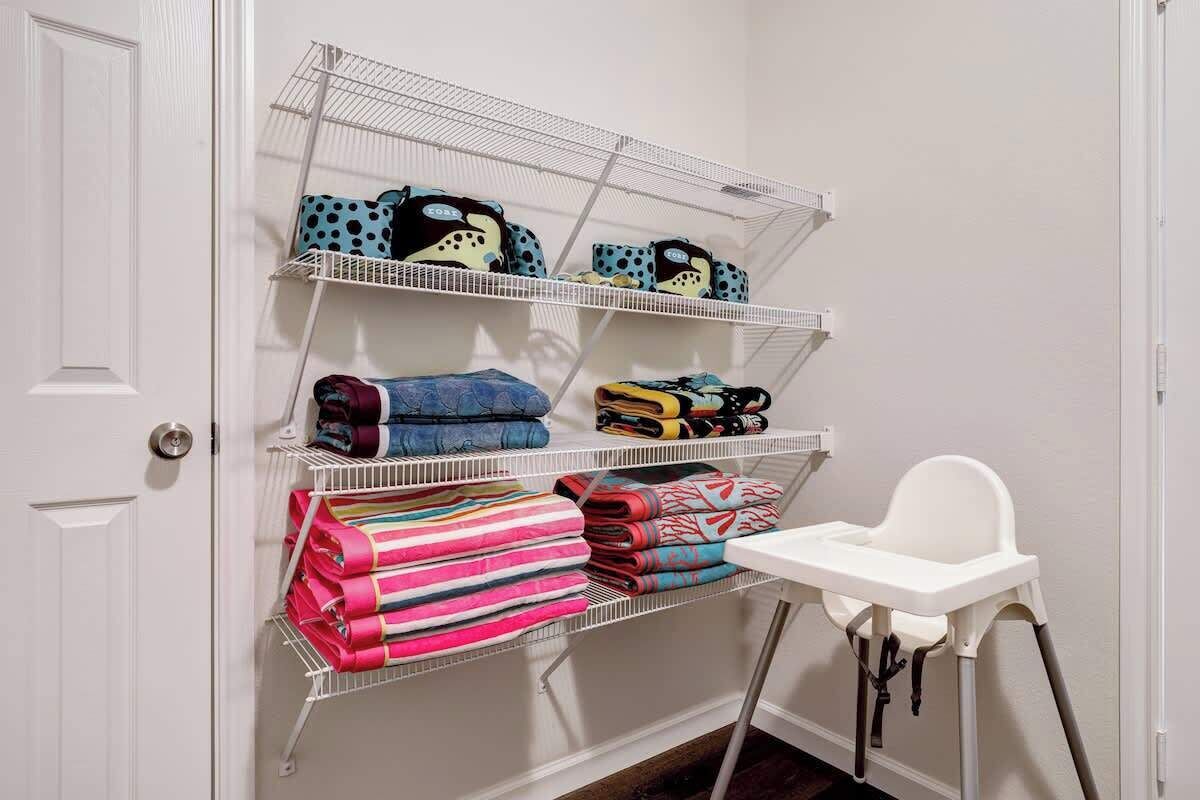 A white door, a white chair, and a metal shelf unit with folded blankets and bags.