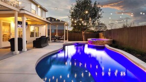 Patio trasero con piscina, terraza techada y luces colgantes.