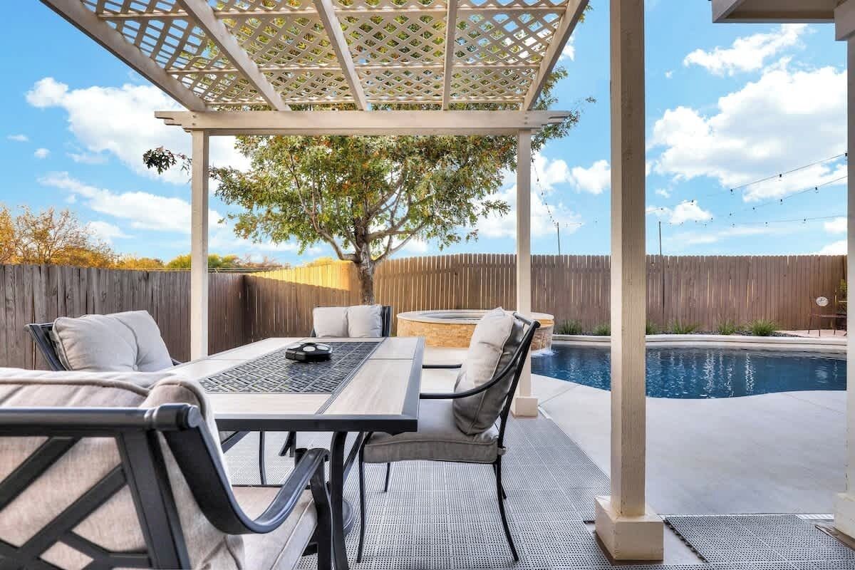 An outdoor patio with a pool, a pergola, and a seating area with a table and chairs.