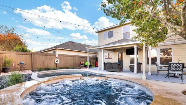 Patio trasero con jacuzzi, mobiliario exterior y valla de madera.