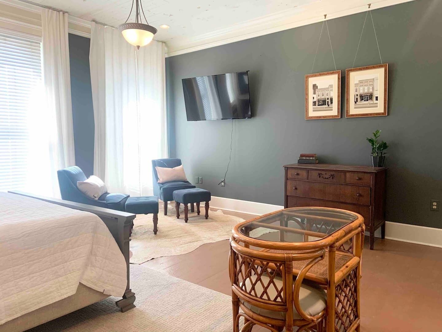 Un dormitorio con cama, dos sillones, una mesita, cómoda y televisor en la pared.