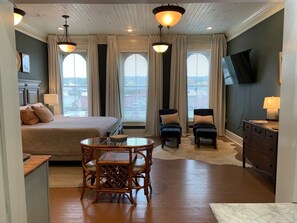 A hotel room with a bed, a dining table with chairs, a TV, and a desk with a lamp. - Archer Suite- Remedies Inn historic downtown (Sweetwater)