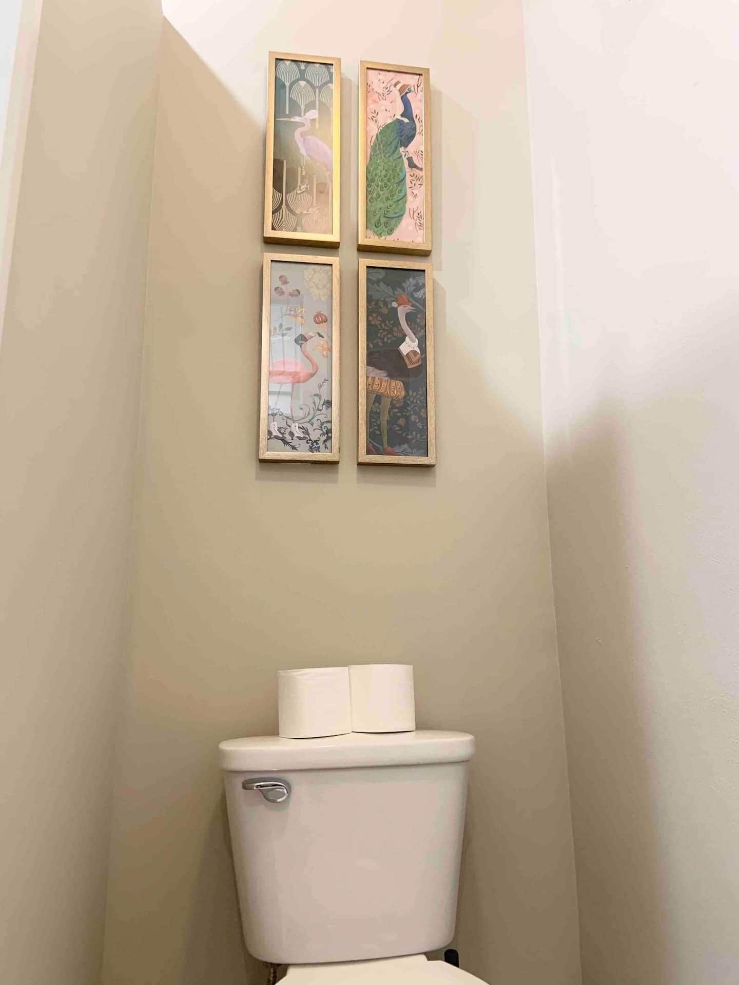 Un baño con inodoro y cuatro obras de arte enmarcadas en la pared.