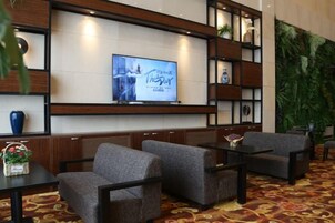Un hall con asientos, televisor y una pared decorada con plantas y estanterías.