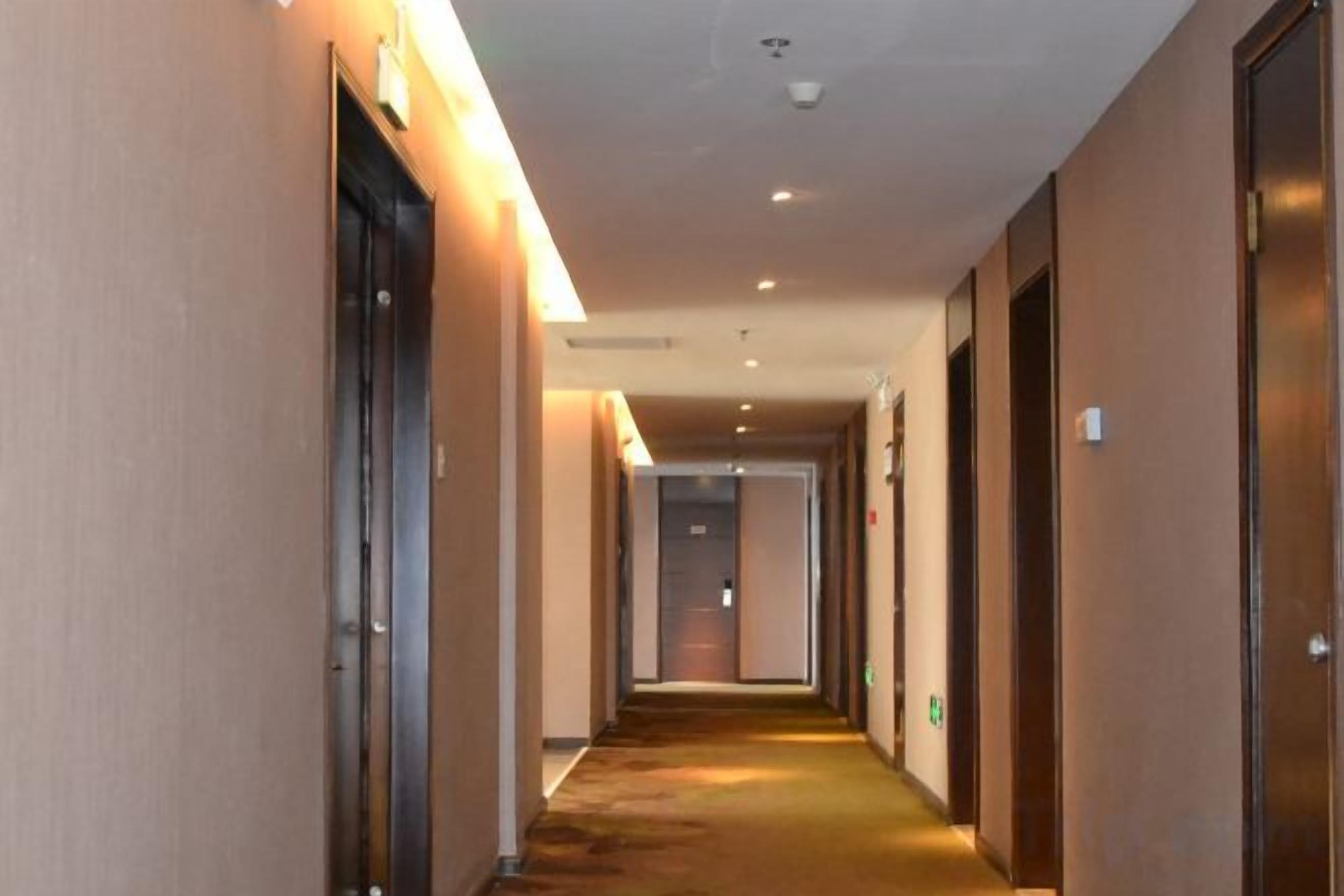 A hotel corridor with doors on both sides, a carpeted floor, and recessed lighting.