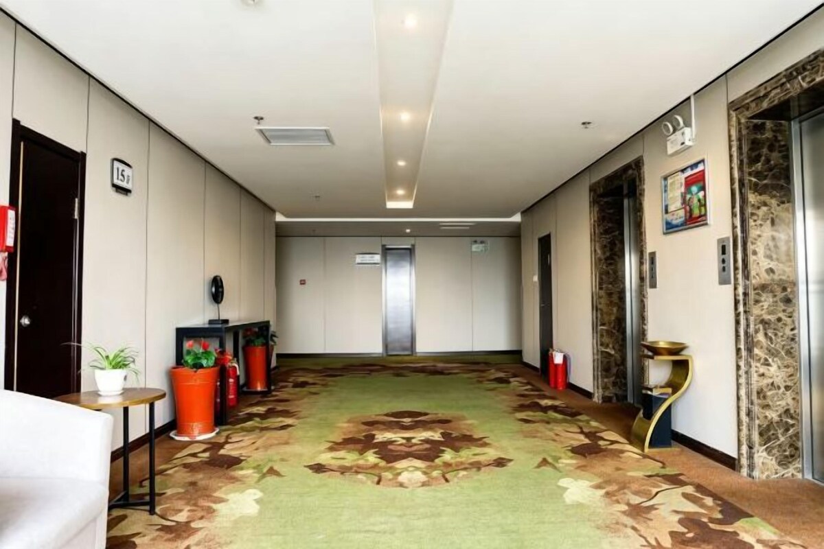 A hotel corridor with a carpeted floor, a reception desk, potted plants, and an elevator.