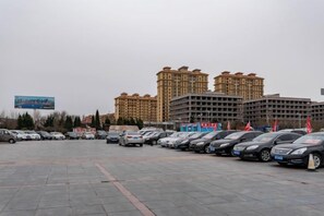 A parking lot with multiple cars and a large building with a billboard in the background. - Ripple Hotel (Weihai Wendeng Bus Station) (Weihai)