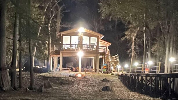 Eine zweigeschossige Holzhütte mit Balkon, umgeben von Bäumen.