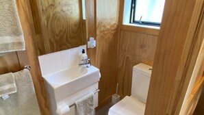 A compact bathroom with a white sink, a toilet, and a window. - Tiny Studio - Near New (Whangamatā)
