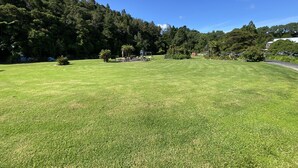A well-maintained grassy area with a gazebo, surrounded by dense trees and a clear blue sky. - Tiny Studio - Near New (Whangamatā)