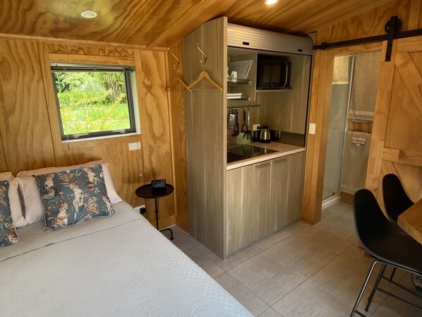 A compact room with a bed, a small kitchenette, and a window with a view of greenery.