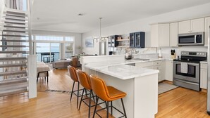 A modern kitchen with white cabinetry, stainless steel appliances, and a large island with bar stools. - The Eastside ~ Modern Coastal Getaway w/ Pool, Private Beach, Sauna and Dock (Colchester)
