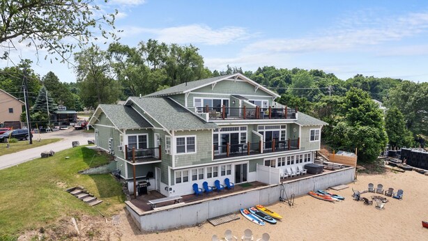 A two-story beach house with a balcony, a covered patio, and a sandy beach area with kayaks and chairs. - The Eastside ~ Modern Coastal Getaway w/ Pool, Private Beach, Sauna and Dock (Colchester)