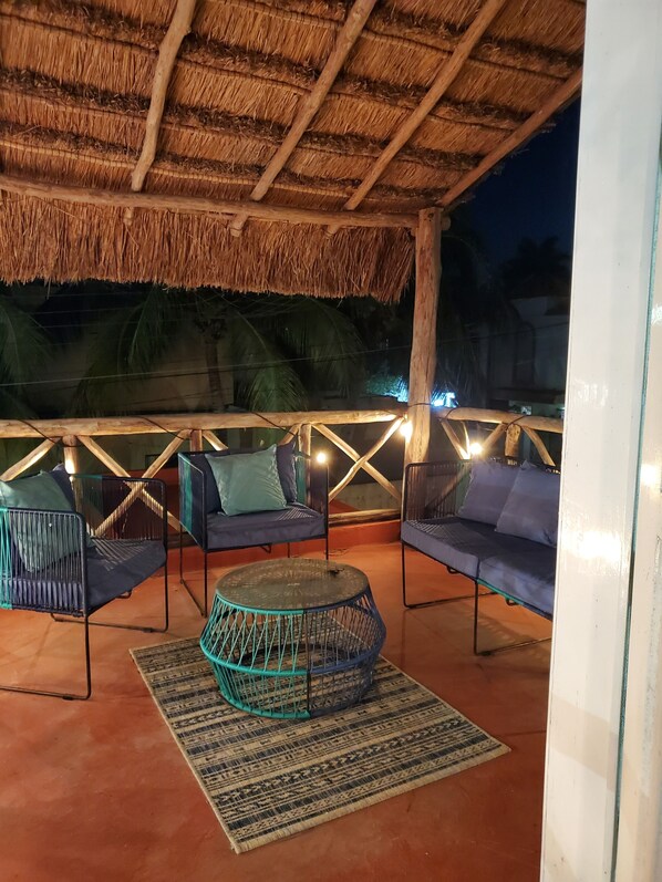 An outdoor seating area with thatched roof, cushioned seating, and a central round table.