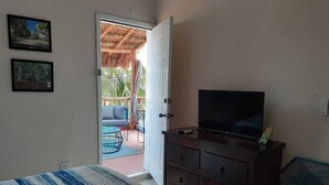 A bedroom with a bed, a TV on a dresser, and a view of an outdoor area with a thatched roof and furniture. - Casa Tranquila- Beautiful House with a Private Pool 2 Blocks from the Ocean (San Miguel de Cozumel)