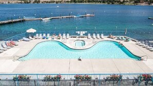 A swimming pool with lounge chairs and umbrellas, surrounded by a fence, with a view of a lake and mountains in the background. - Lake Chelan Waterfront Resort Home- Pool, Boat -STR-0290 (Chelan)
