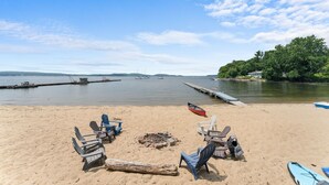 A beach with lounge chairs, a fire pit, and a canoe. - The Westside - Hot tub, Private Beach & Dock. Pet-friendly! (Colchester)