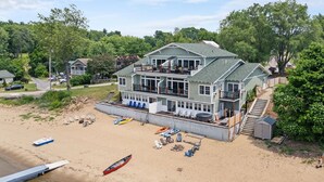 A large two-story house with a balcony, located near a beach with several boats and beach chairs. - The Westside - Hot tub, Private Beach & Dock. Pet-friendly! (Colchester)
