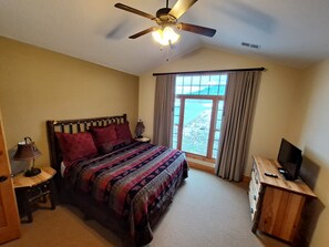 A bedroom with a bed, a ceiling fan, a nightstand, a TV, and a window with curtains.