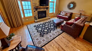A cozy living room with a stone fireplace, wooden flooring, a patterned rug, leather sofas, and a television mounted on the wall. - Serendipity 22 (Branson)