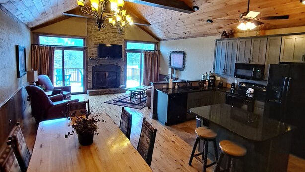 A spacious living area with a wooden ceiling, a dining table with chairs, a fireplace, and a kitchen area with a bar. - Serendipity 22 (Branson)