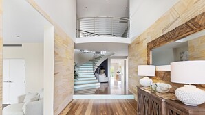 A spacious living area with a curved sofa, a wooden console table with decorative items, and a staircase leading to an upper level. - Grandview - Luxurious Entertainer with Spectacular Views (Nelson Bay)