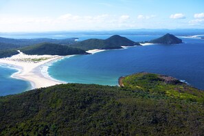 A coastal landscape with a beach, forested hills, and a clear view of the ocean. - Grandview - Luxurious Entertainer with Spectacular Views (Nelson Bay)