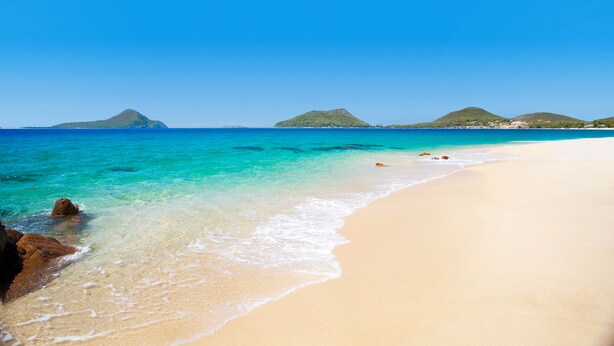 A beach with clear turquoise water, sandy shore, and distant green hills. - Grandview - Luxurious Entertainer with Spectacular Views (Nelson Bay)
