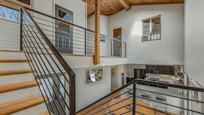 Un intérieur à plusieurs niveaux comprenant un escalier, des poutres en bois, un coin cuisine et un espace repas.