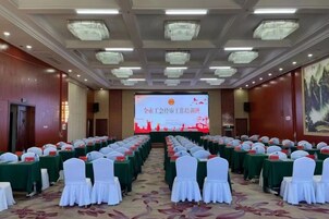 Un salón de conferencias con filas de mesas, sillas y una pantalla de proyección.