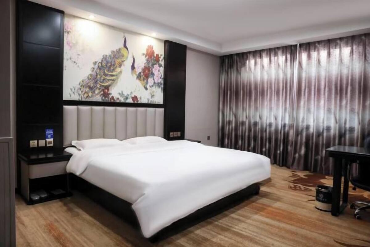 Habitación de hotel con una cama grande, una mesita de noche, un escritorio y un cuadro grande en la pared.