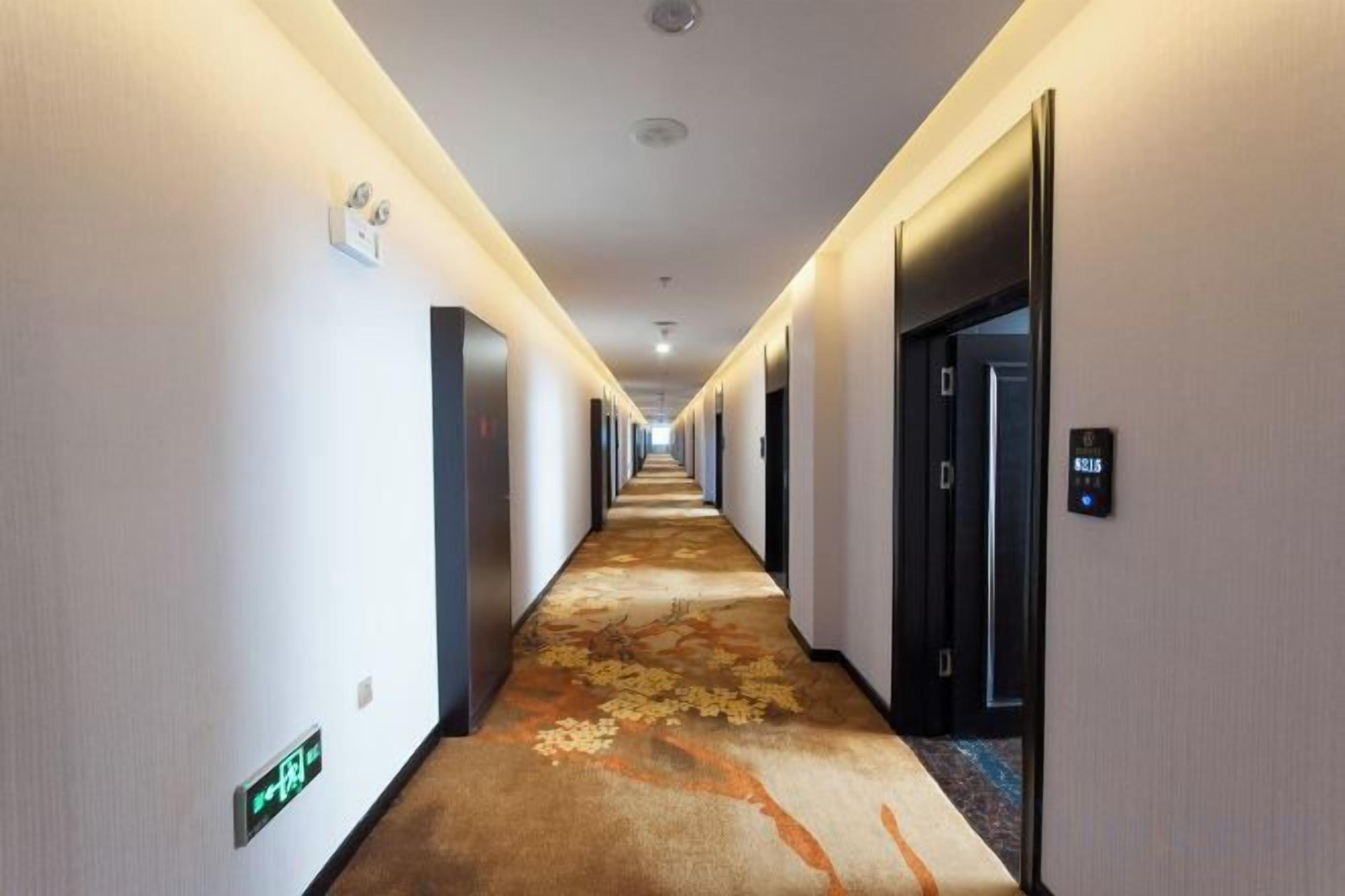A hotel hallway with a carpeted floor, doors on both sides, and a sign indicating the direction to the elevators.