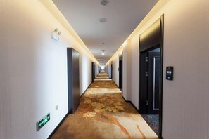 A hotel hallway with a carpeted floor, doors on both sides, and a sign indicating the direction to the elevators. - He Qi Boutique Hotel (Harqin Banner)