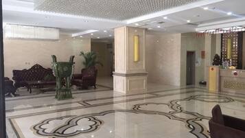 A lobby with a marble floor, sofas, a reception desk, and a decorative pillar.