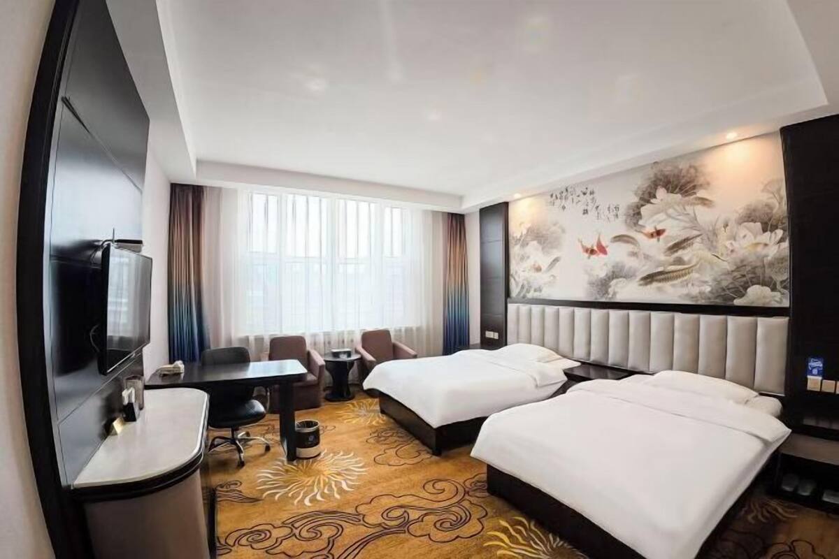 Habitación de hotel con dos camas, un escritorio, un televisor y un cuadro grande en la pared.