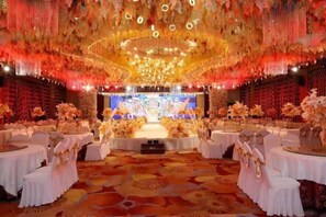 Un salón de banquetes con mesas redondas, un escenario y suelo alfombrado.