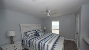 A bedroom with a bed, nightstand, lamp, ceiling fan, and a window with a view.