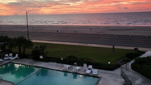 A sunset view from a pool area with lounge chairs and a view of the beach and ocean.