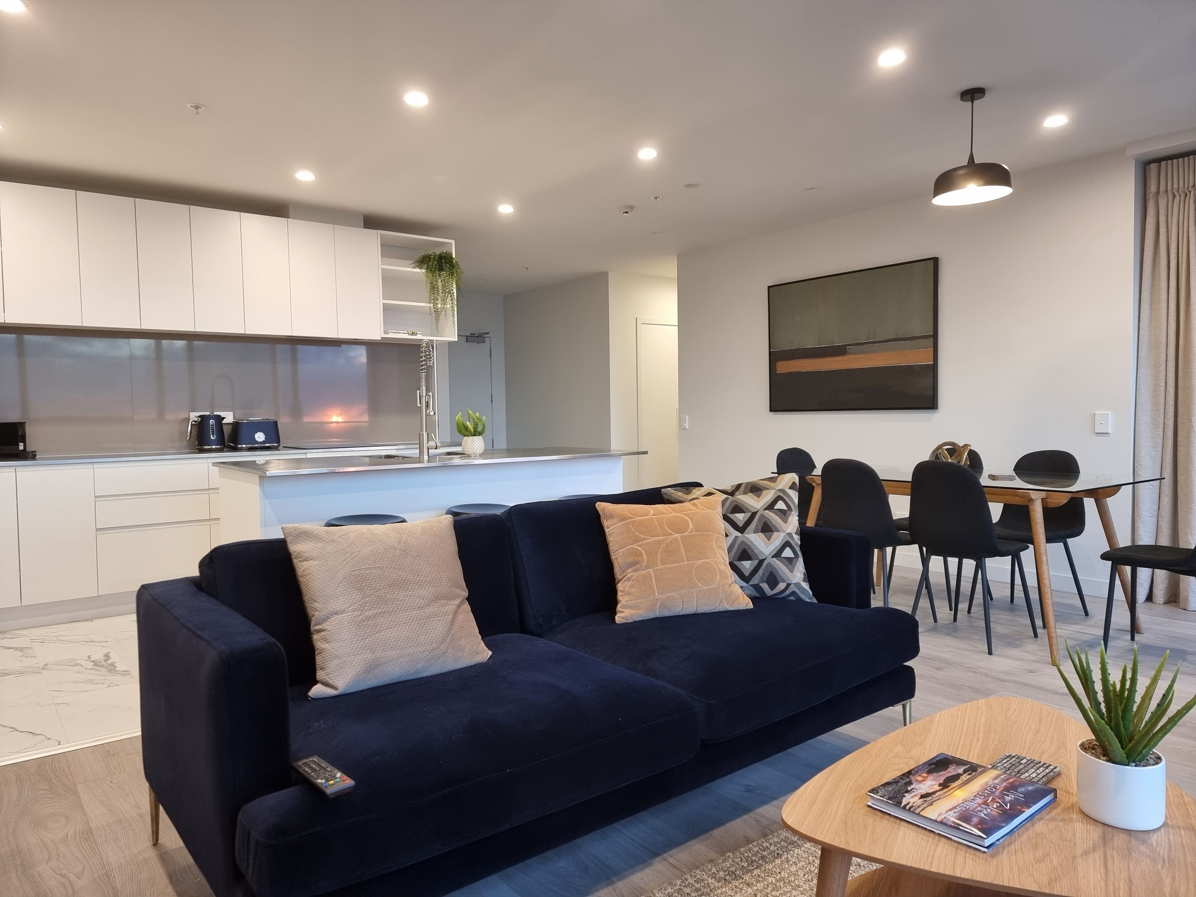 A modern living room with a dark blue sofa, a coffee table, and a dining area with a table and chairs.