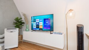 A modern living room with a flat-screen TV mounted on a white wall, a standing heater, a floor lamp, and a small plant.