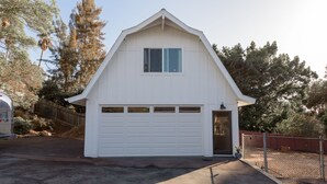 A white single-story house with a garage, surrounded by trees and a fenced yard.