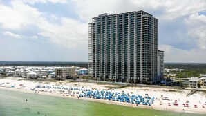 Un grand hôtel avec vue sur la plage, doté de nombreux balcons et donnant accès à une plage équipée de parasols.