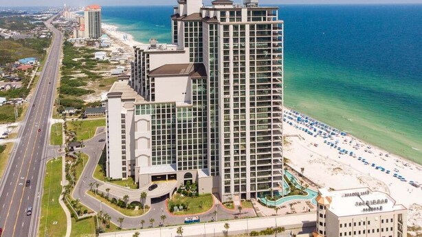 Un hôtel de grande hauteur offrant une vue sur la plage, comprenant de nombreux étages et situé à proximité d’une route.