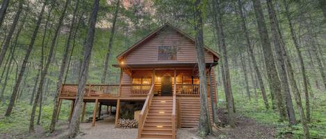 Une cabane en bois avec un escalier menant à l’entrée, entourée d’une forêt.