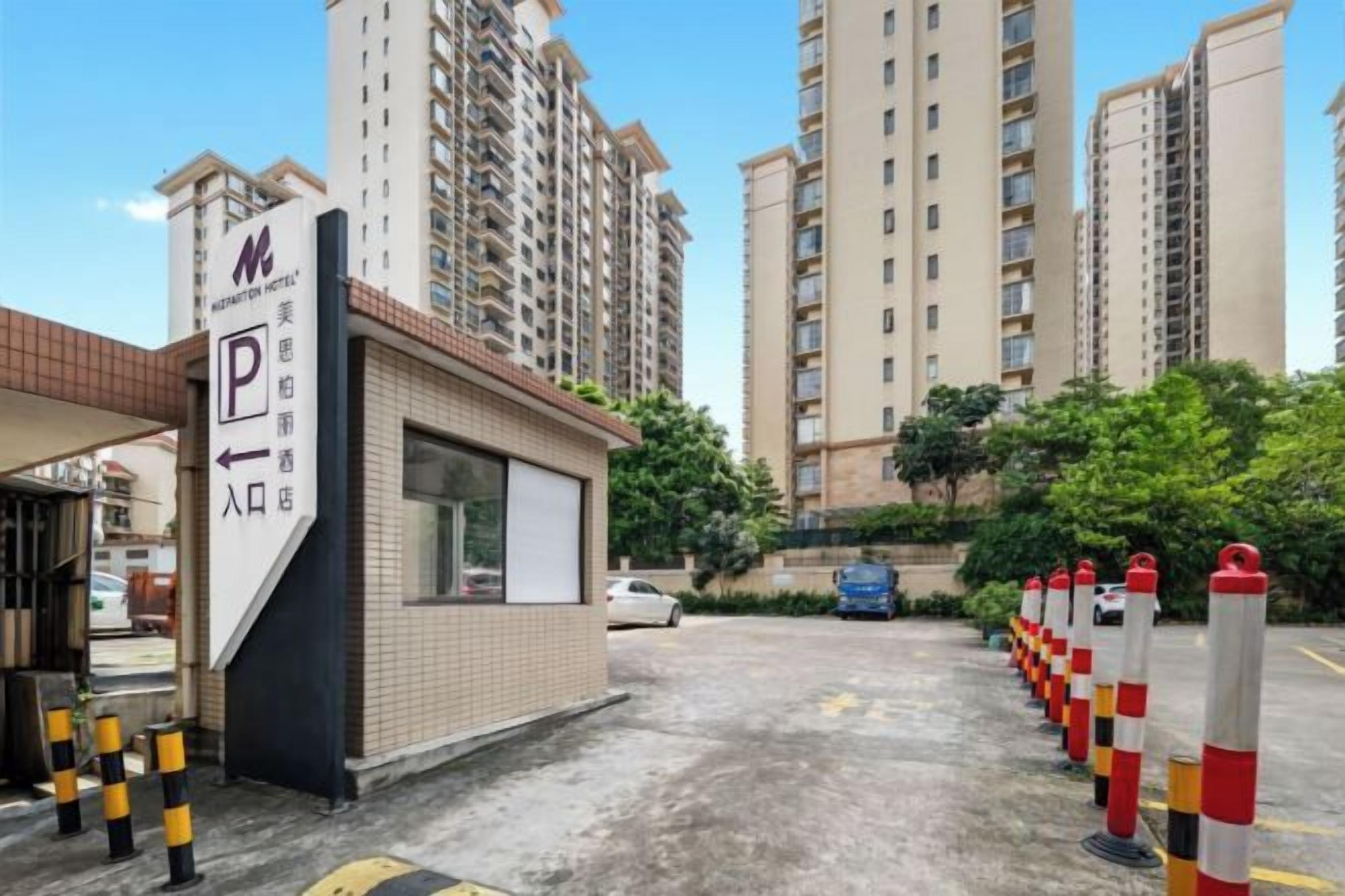 A hotel entrance with a parking sign, a small reception booth, and tall residential buildings in the background.