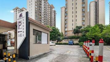 A hotel entrance with a parking sign, a small reception booth, and tall residential buildings in the background.