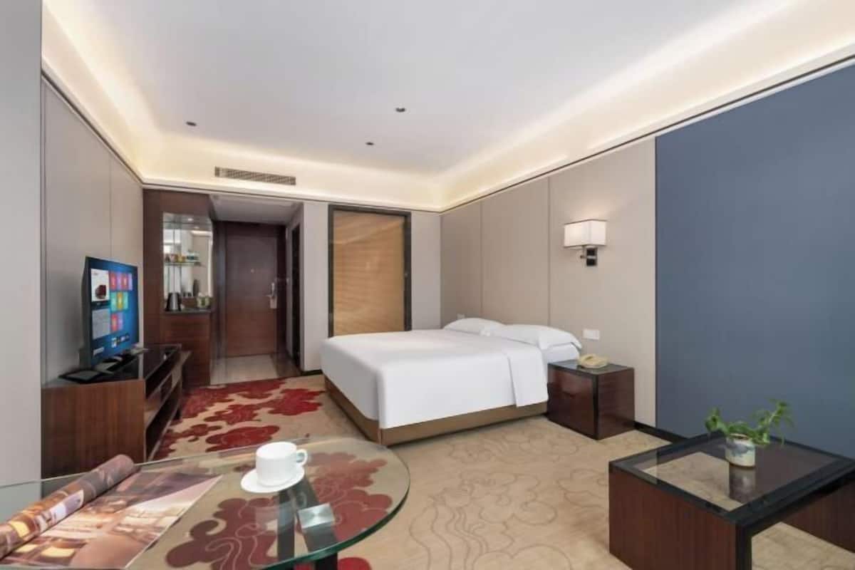 Ein Hotelzimmer mit Bett, Nachttisch, Lampe, Fernseher und einem Glastisch.