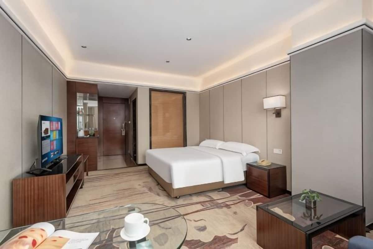 Ein Hotelzimmer mit einem Bett, einem Schreibtisch mit Lampe, einem Fernseher und einem kleinen Tisch mit Tasse und Pflanze.